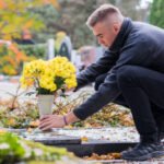 Man at headstone with mixed flower arrangement